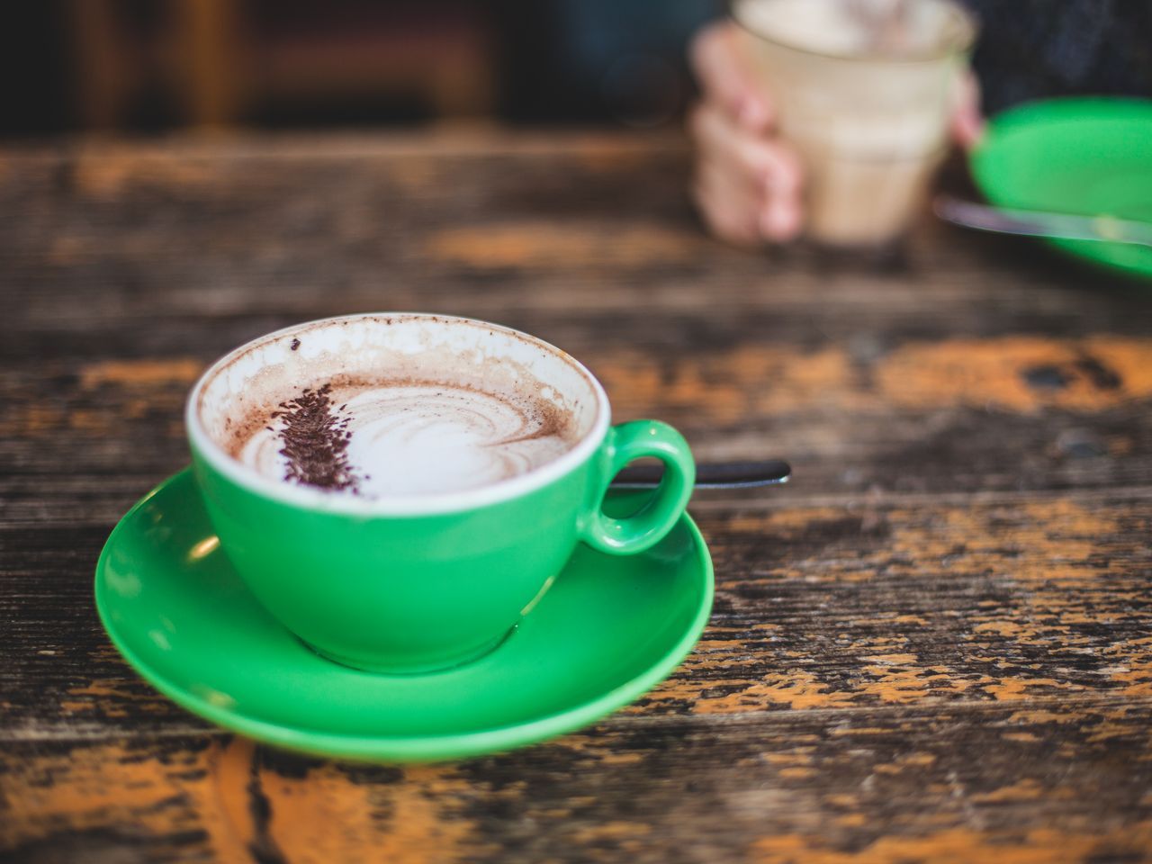 An espresso in a green cup and saucer on a wooden café table